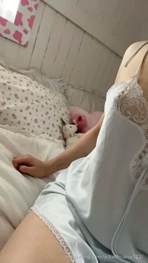 Woman in light blue lace pajamas lying in bed with floral bedding and stuffed toys.