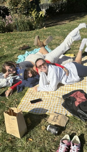 Three women in casual clothes on picnic blanket in park.