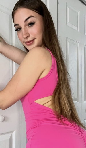 Brunette in pink tank top and leggings against door.