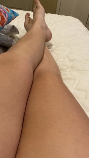 Person's legs resting on bed with colorful pillow nearby.
