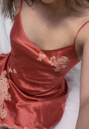 Woman in red satin dress with lace details, sitting on white surface.