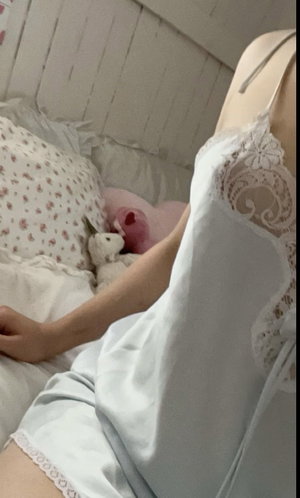 Woman in white lace pajamas lying in bed with stuffed animals.