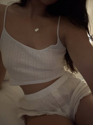 Woman in white crop top and shorts, sitting indoors, dark hair, necklace visible.