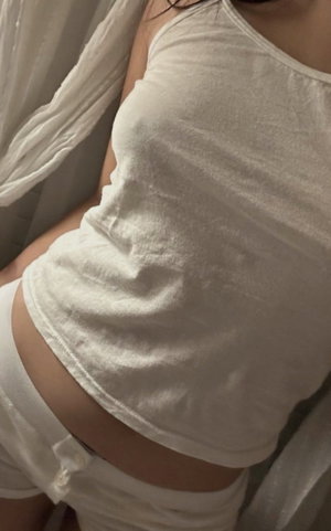 Woman in white crop top and underwear, close-up of torso, indoor setting.