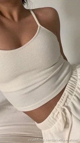 Woman in white ribbed crop top and matching pants, indoor setting.