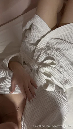 Woman in white robe lying on bed, hand resting on thigh, wearing delicate anklet.