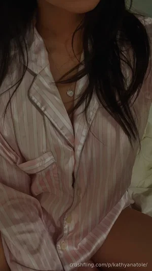 Woman in pink striped pajama shirt, sitting indoors, dark hair, necklace visible.