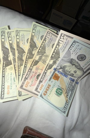 US $100 bills fanned on bed with wallet.