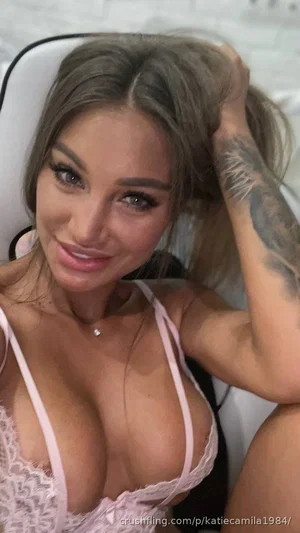 Woman with tattooed arm in pink lace lingerie, sitting indoors.