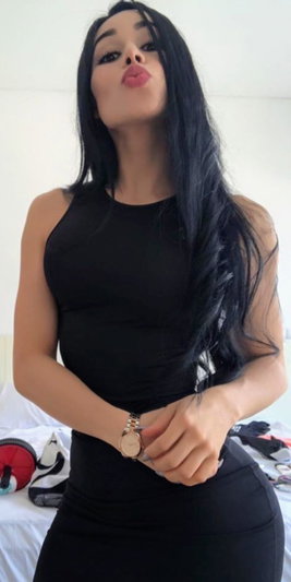 Woman with long black hair in black dress posing indoors.