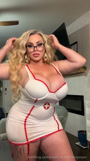 Woman with blonde curls in white nurse-themed dress with red trim, posing indoors.