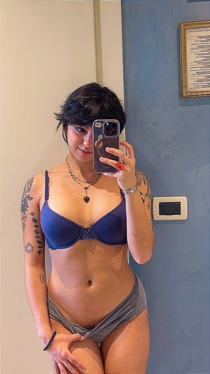 Short-haired woman in blue bra taking mirror selfie indoors.