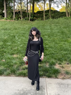 Woman with dark hair in black dress standing outdoors.