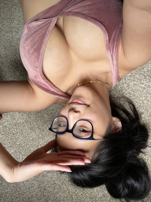 Woman with dark hair and glasses lying on carpet, wearing pink top, hand near face.