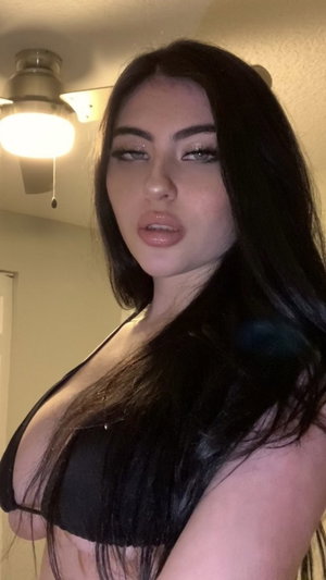 Woman with long black hair wearing black bra, indoors under ceiling light.