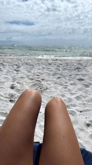 Tanned thighs on sandy beach with ocean background.