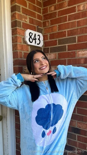 Woman in blue cloud-themed onesie posing by brick wall with house number 843.