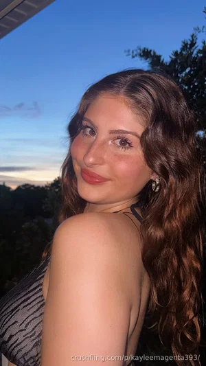 Woman with long brown hair in a patterned top, outdoors at dusk.