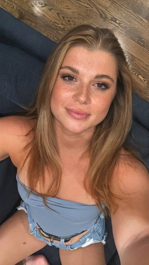 Woman with long brown hair in blue top and denim shorts lying on dark surface.
