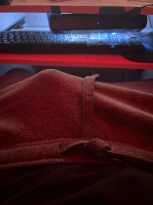 Red fabric garment on lap with computer desk behind