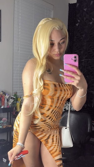 Woman with blonde hair in tiger-print dress taking mirror selfie indoors.