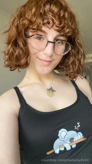Woman with curly brown hair and glasses wearing a black tank top with a koala graphic, indoors.