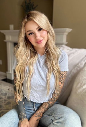 Blonde woman with tattoos wearing t-shirt and jeans indoors.