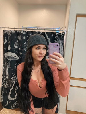 Woman with long hair in beanie taking bathroom mirror selfie.