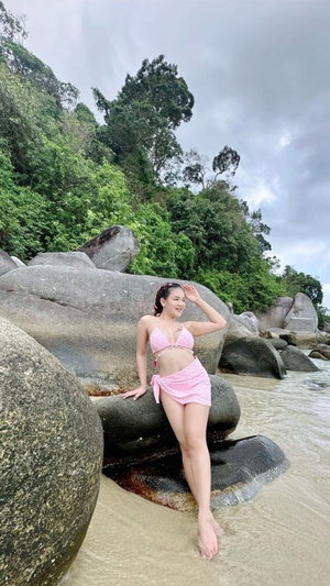 Asian woman in pink bikini on rocks by the sea