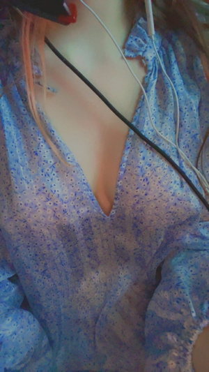 Woman with pink hair in blue floral top wearing earphones.