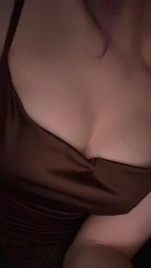 Woman in brown top showing cleavage in dim light.
