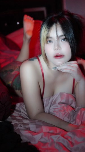 Asian woman with two-tone hair in red top on bed.
