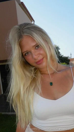 Blonde woman in white crop top outdoors, smiling at camera.
