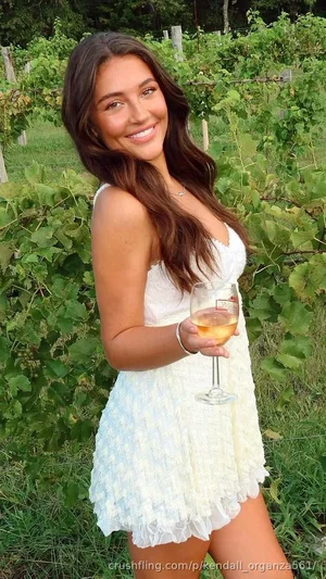Woman in white dress holding wine glass in vineyard, smiling at camera.