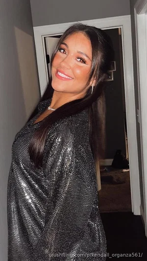 Woman with long dark hair in a sparkly black top, smiling in a hallway.