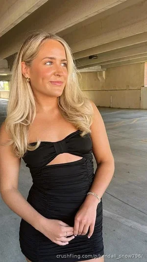 Woman with blonde hair in black cutout dress standing under concrete structure.