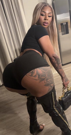 Blonde woman in black outfit posing indoors with tattoos.