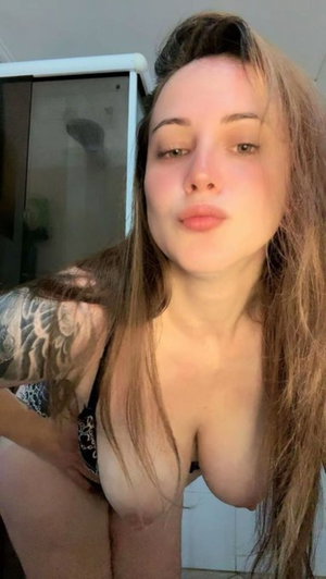 Woman with long hair and tattooed arm in black lingerie, posing indoors.