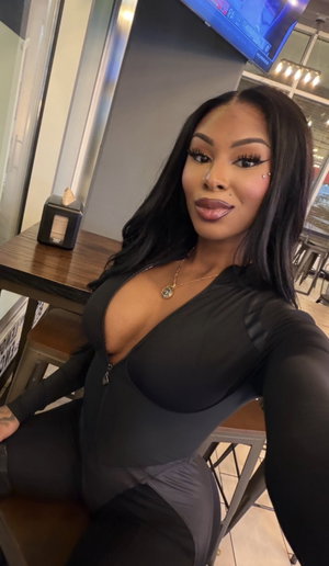 Woman in black bodysuit taking selfie at restaurant table.