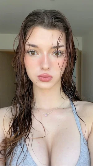 Woman with wet hair wearing a gray tank top, indoors, facing camera.