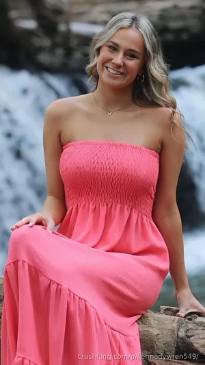Woman in pink strapless dress sitting by waterfall, smiling.