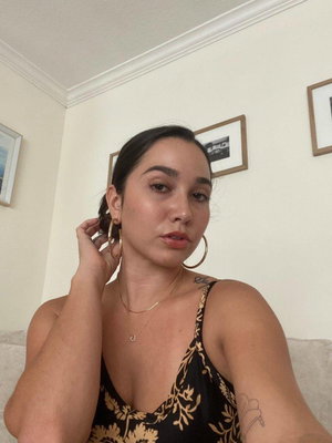 Woman with dark hair in floral top taking selfie indoors.