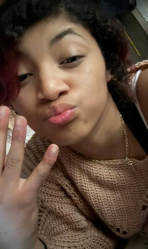 Curly-haired woman in beige sweater, duck face, peace sign.