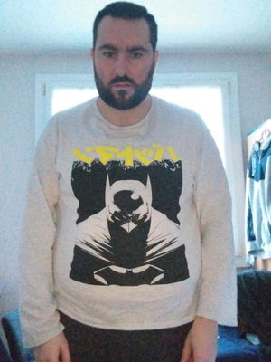 Man with beard wearing Batman graphic long-sleeve shirt indoors.