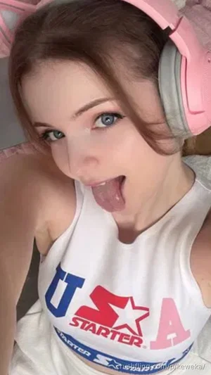Woman with blue eyes and pink headphones wearing a white USA Starter tank top, sticking out tongue.