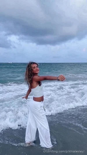 Woman in white crop top and pants standing in ocean waves at beach.
