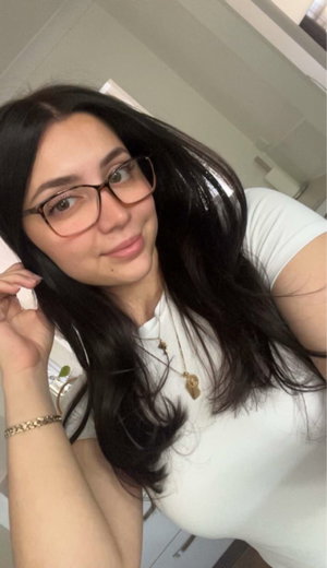 Woman with long dark hair and glasses wearing white t-shirt indoors.