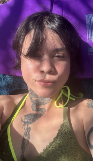 Woman with neck tattoo wearing green lace top outdoors.