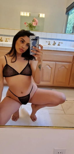 Woman in black lingerie taking mirror selfie in bathroom.
