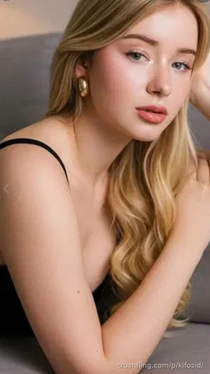 Blonde woman in black top posing on gray couch, indoor setting.